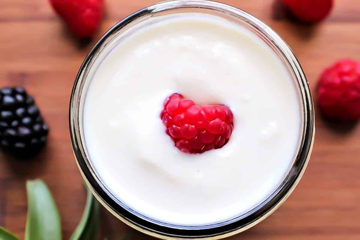 A top view of a mason jar filled with soy yogurt with a red raspberry in the middle.