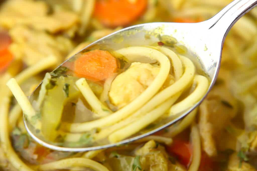 A close up of a spoonful of vegan noodle soup with noodles, celery and carrots in it.