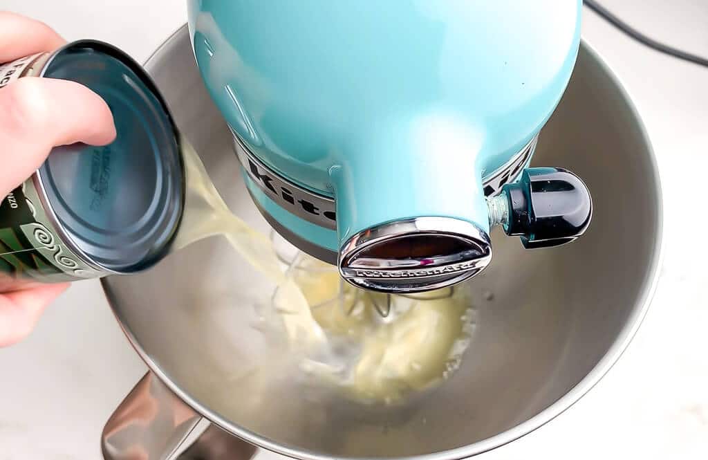 Pouring a can of chickpea liquid into a mixing bowl to make vegan whipped cream.