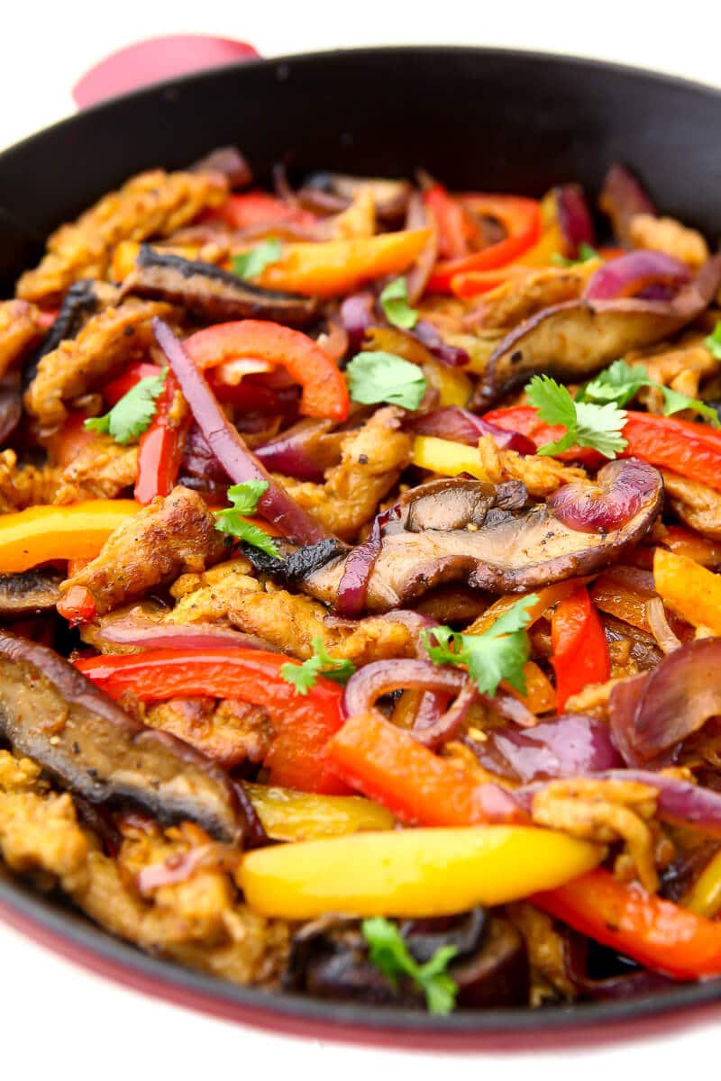 A close up of a skillet filled with onions, peppers, mushrooms, and soy curls cooked with fajita spices.