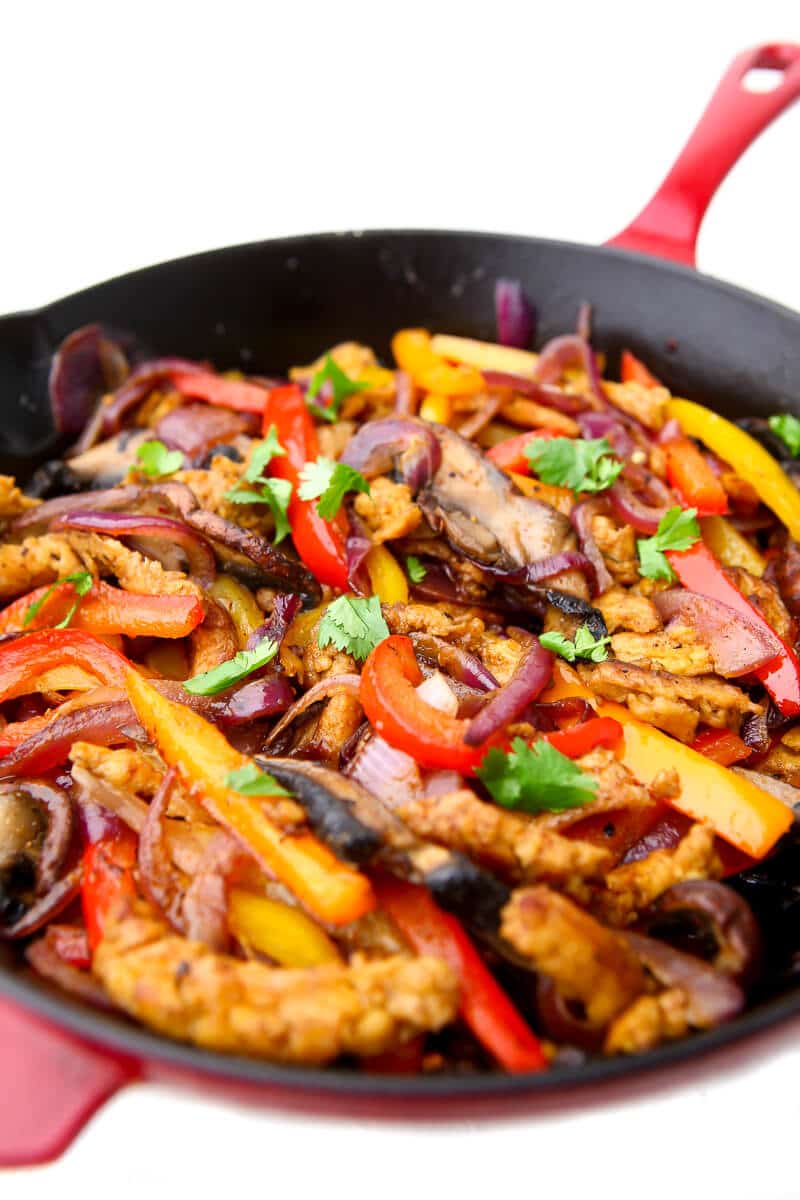 A red skillet filled with cooked veggies and soy curls to make vegan "chicken" fajitas.