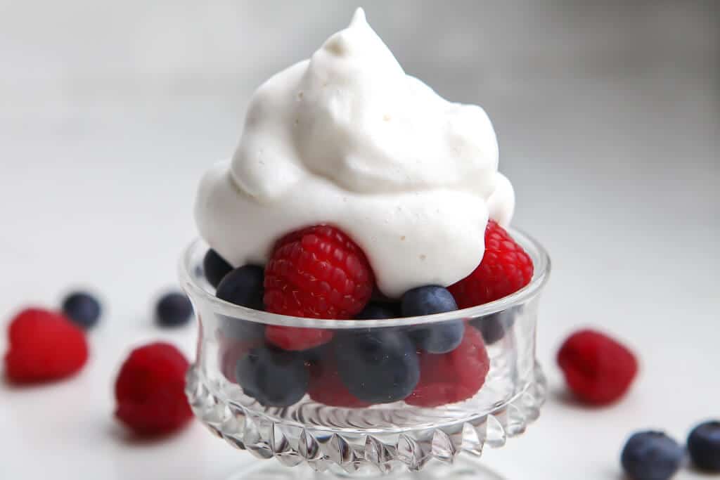 A bowl of berries topped with vegan whipped cream.