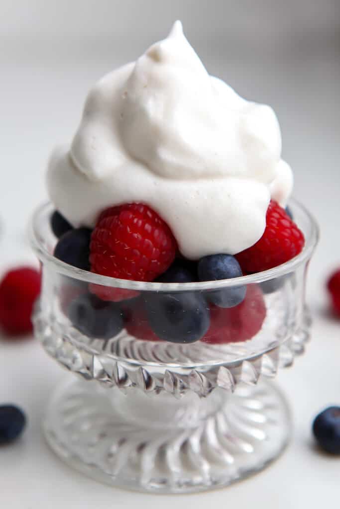 A glass bowl filled with blueberries and raspberries topped with aquafaba whipped cream. 