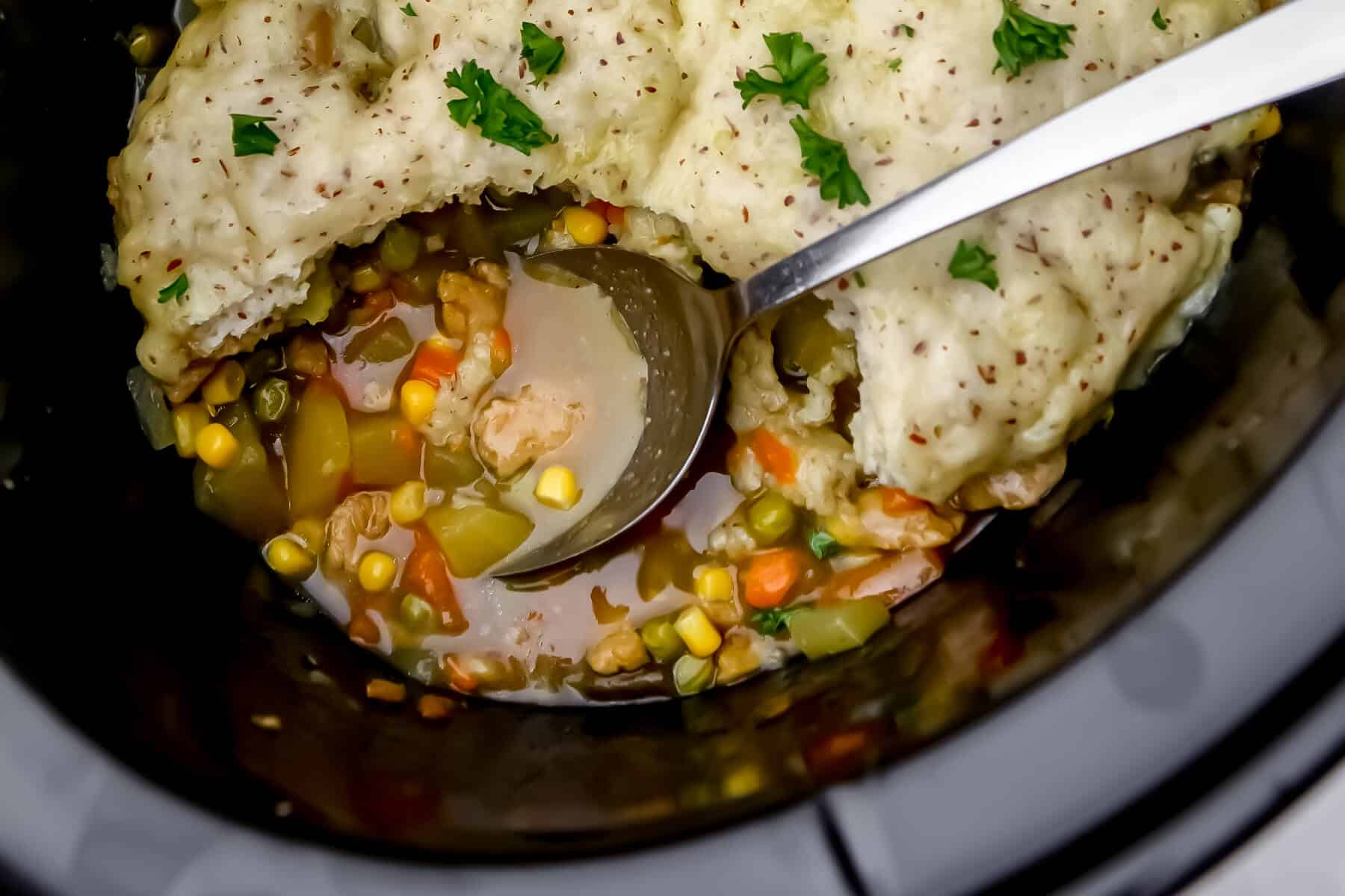 A close up of vegan chicken pot pie with biscuit topping being scooped out of a crock pot.