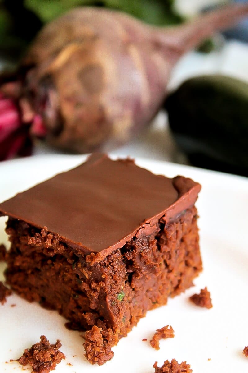 A veggie brownies made with zucchini and beets on a white plate with beets behind it.