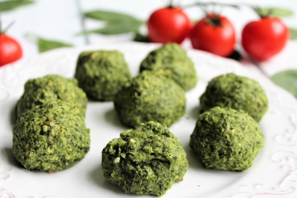 Gluten free, vegan spinach balls on a plate with tomatoes in the background.