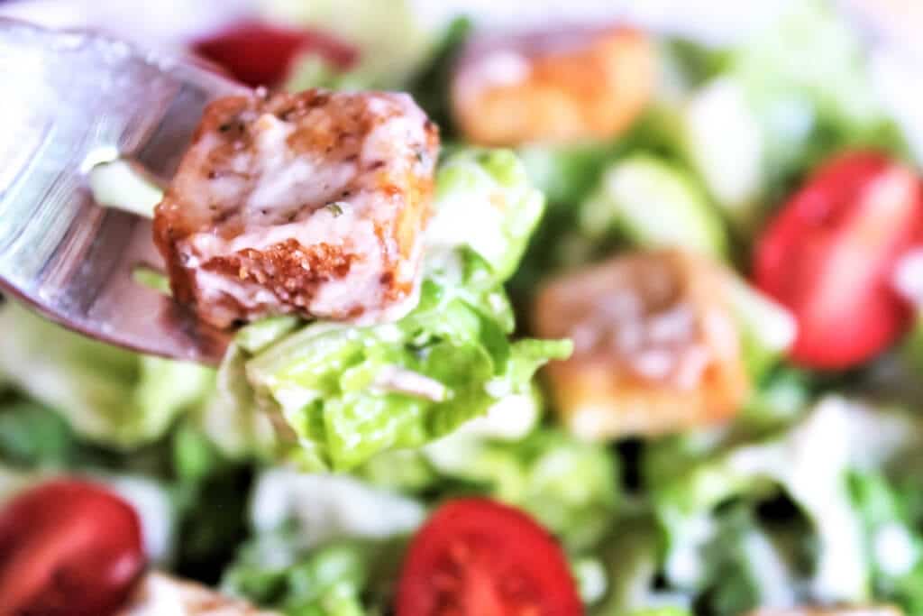 A bite of vegan Caesar salad with croutons and cherry tomatoes.