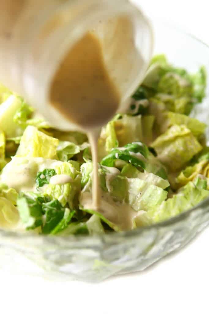 Vegan Caesar dressing being poured over a bowl of Romaine lettuce.