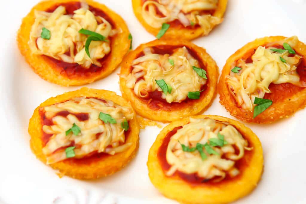 A close up of plant based polenta pizza rounds on a white plate.