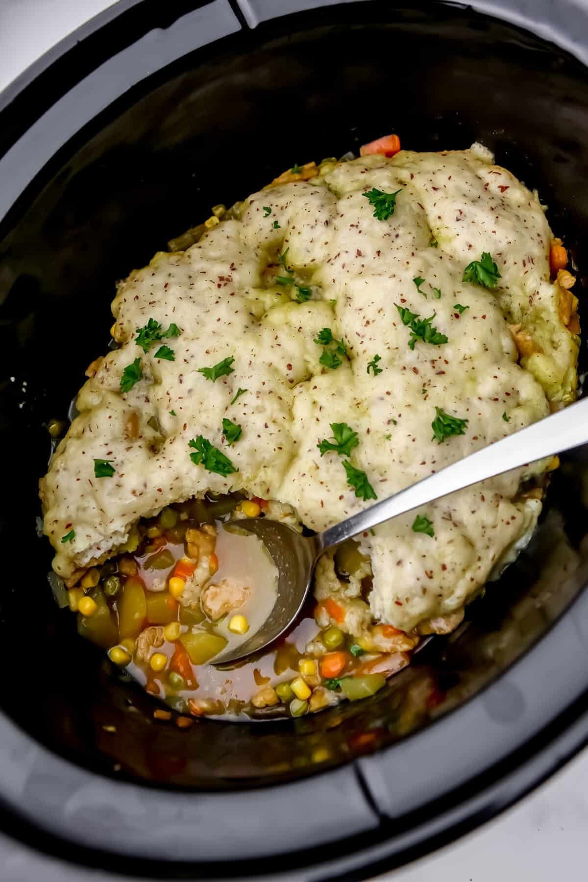 A vegan pot pie in a slow cooker with a scoop taken out of it.