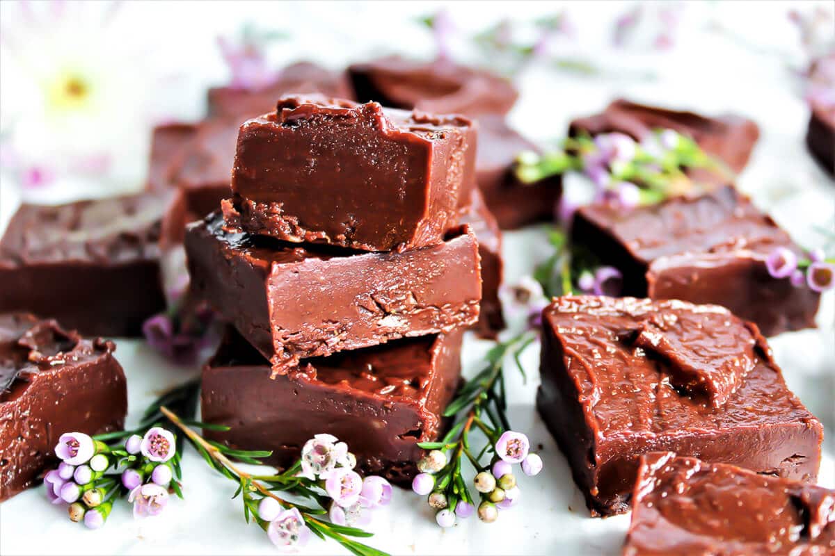 Squares of healthy freezer fudge made with almond butter with small pink flowers around it.