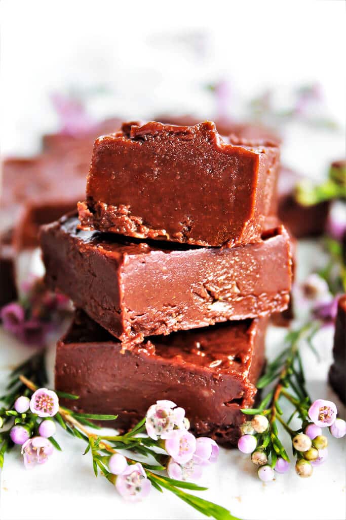 A stack of 3 pieces of healthy fudge made with almond butter with pink flower around it.