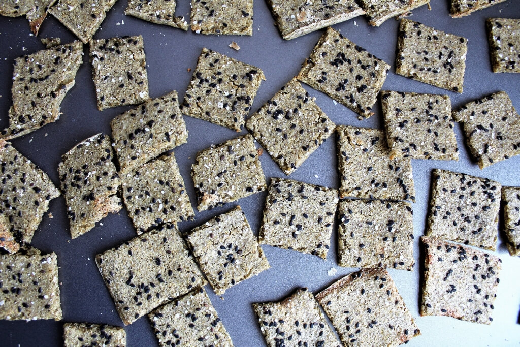 Baked homemade quinoa crackers with black sesame seeds on a cookie sheet.
