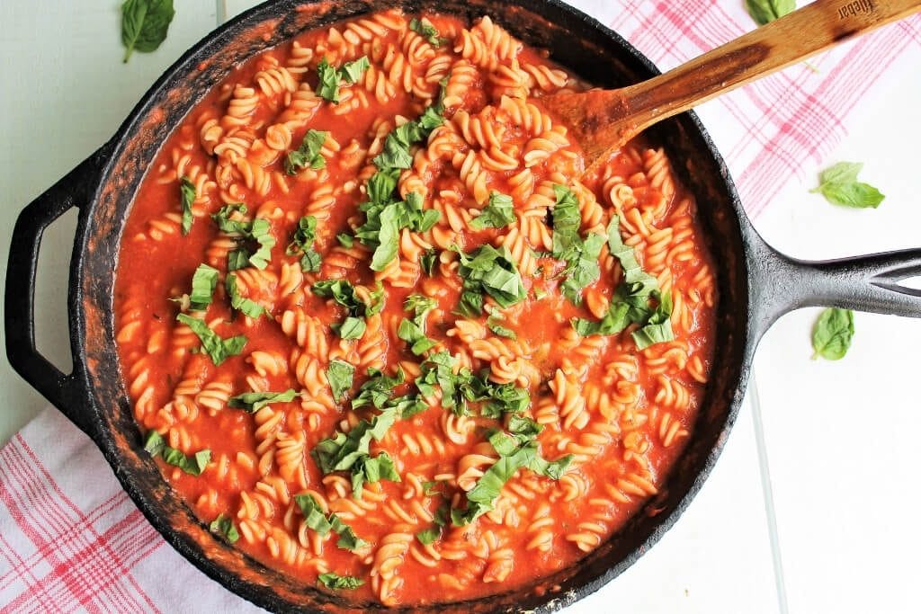An Iron skillet full of pasta with vegan vodka sauce with cream and basil sprinkled on top ready to serve. 