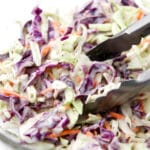 A close up of vegan coleslaw in a bowl with tongs scooping some out.
