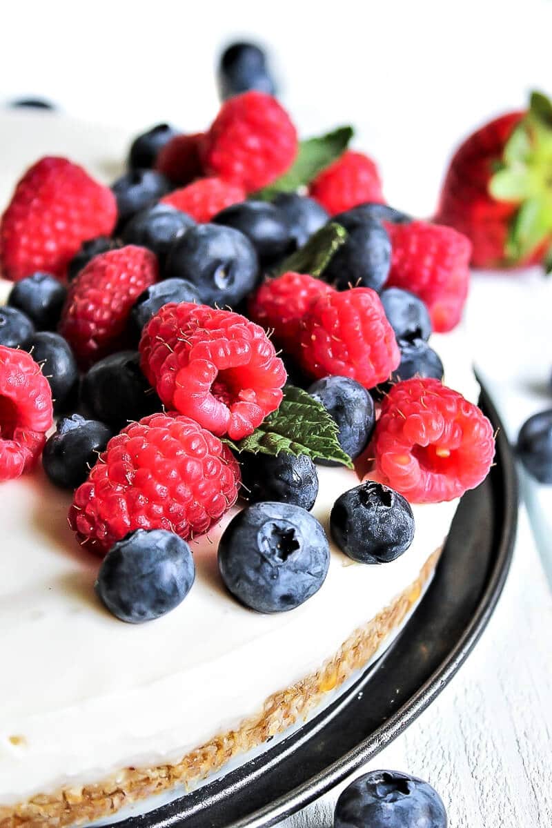 A vegan cheesecake topped with blueberries and raspberries.