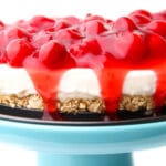 A vegan cheese cake made with vegan cream cheese and topped with cherry pie filling on a blue cake stand.