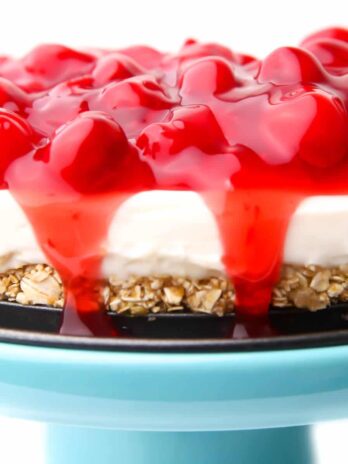 A vegan cheese cake made with vegan cream cheese and topped with cherry pie filling on a blue cake stand.