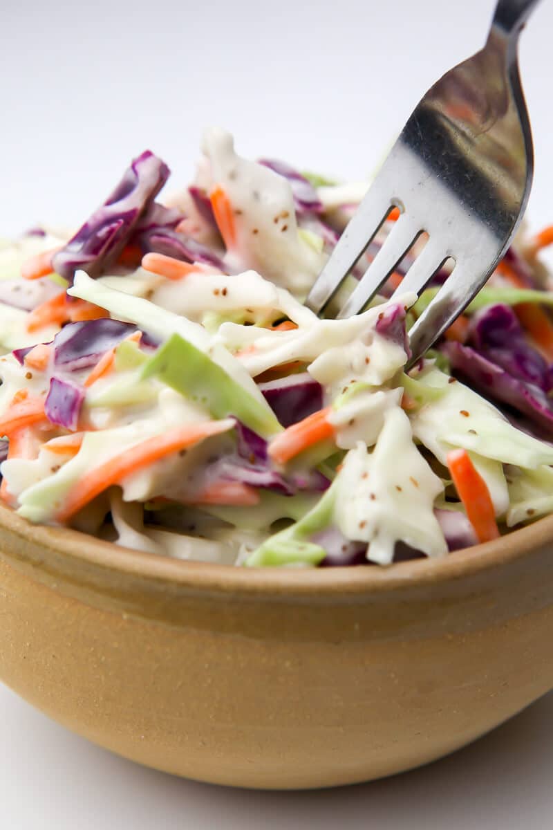 A brown bowl filled with coleslaw made with green and purple cabbage, carrots and vegan mayo.