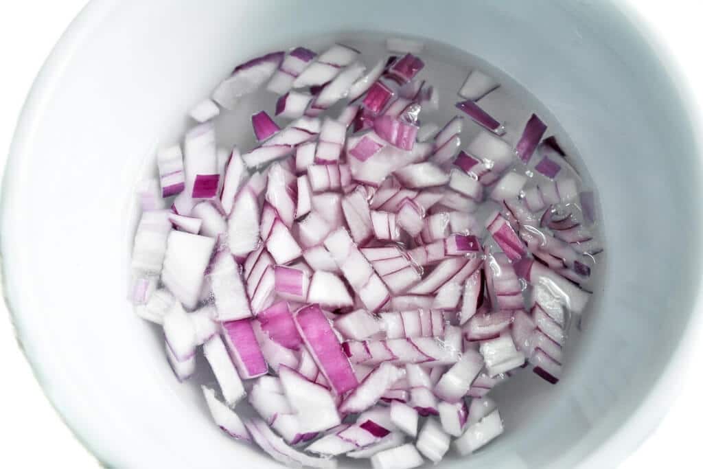 A bowl of diced red onions soaking in water to mellow the flavor.