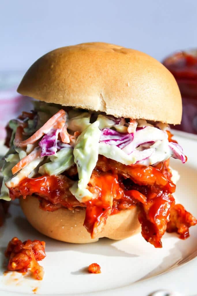 A vegan pulled pork sandwich made with Butler soy curls and sugar free barbecue sauce on a white plate with a blue background.