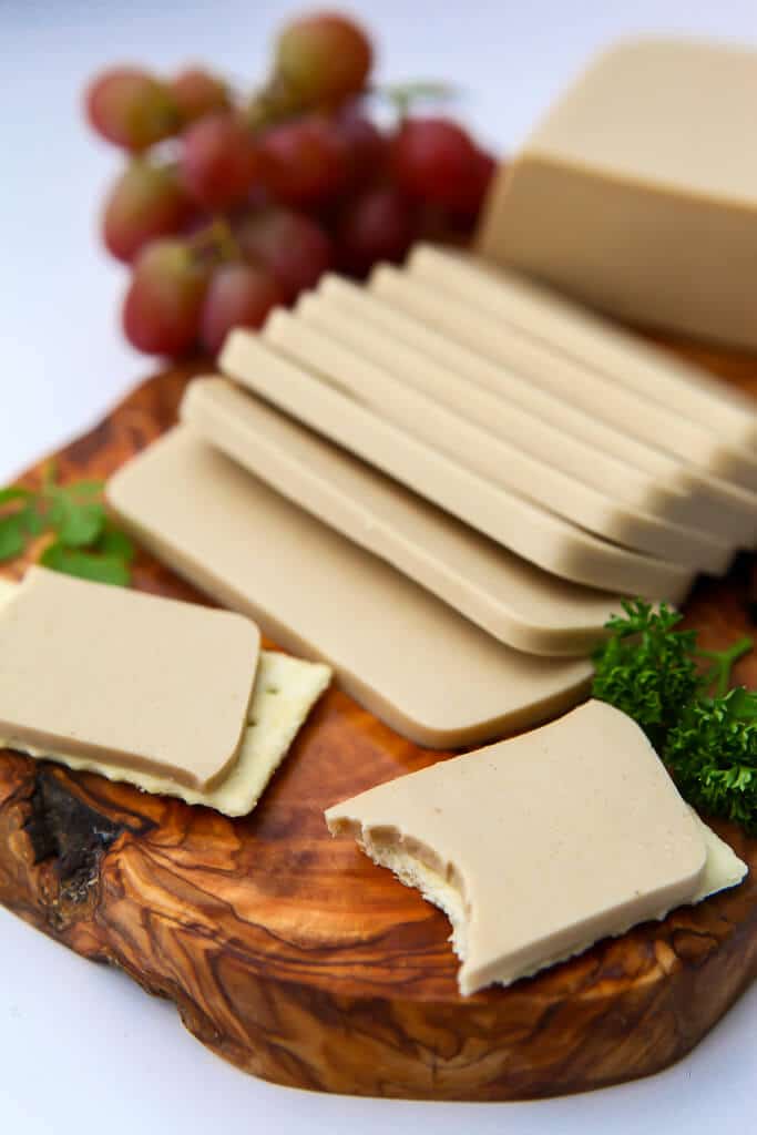 A cheese plate with vegan smoked Gouda on crackers with a bite taken out of one of them.