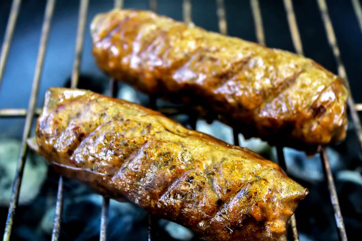 Two vegan sausages being grilled over a charcoal grill.