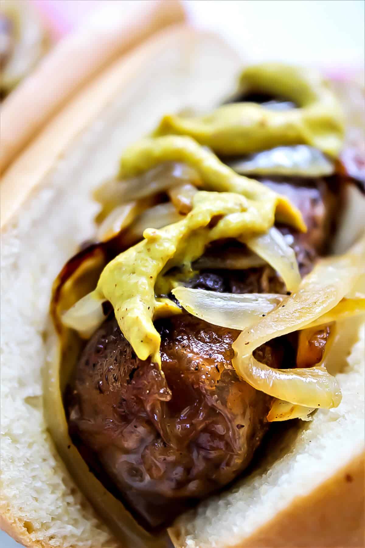 Vegan beer brat sausage with fried onions and mustard.