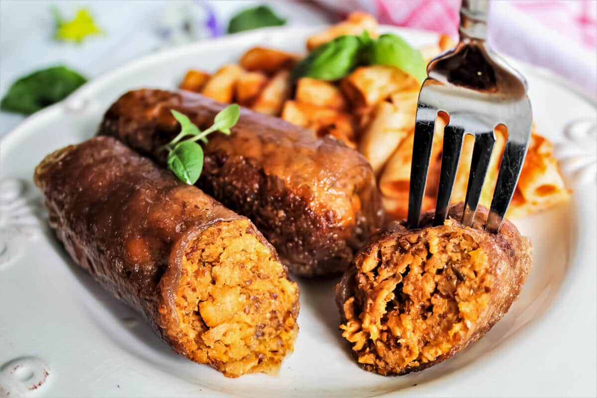 A homemade vegan Italian style sausage with a fork sticking in it with pasta on the side.