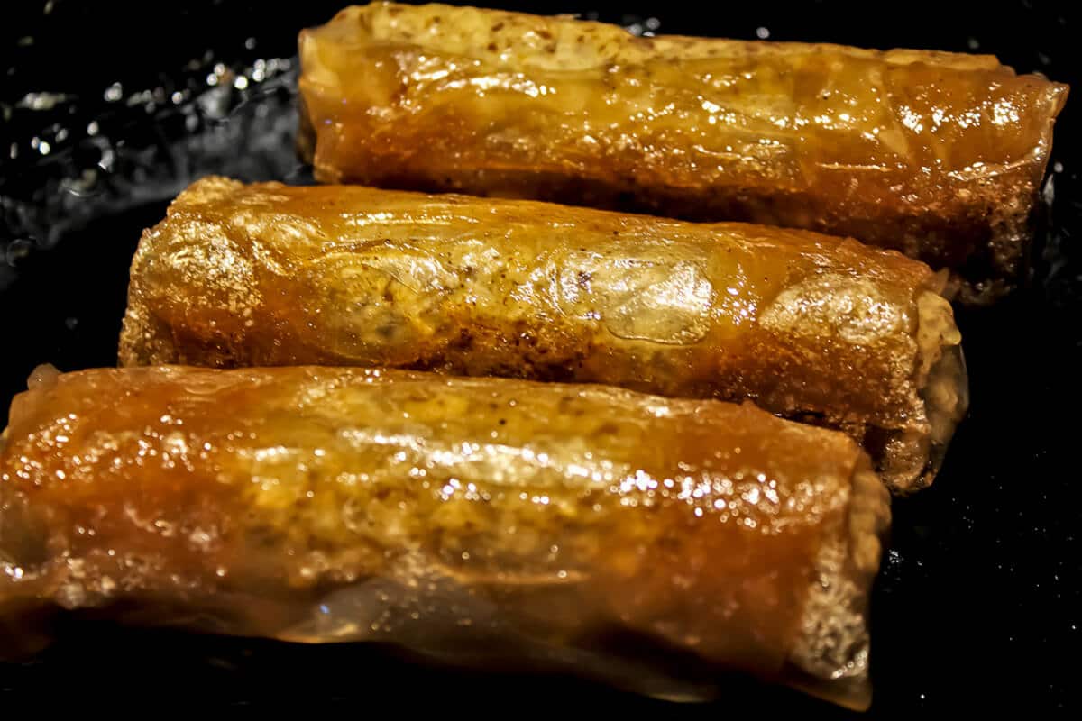 Vegan sausages frying in an iron skillet.