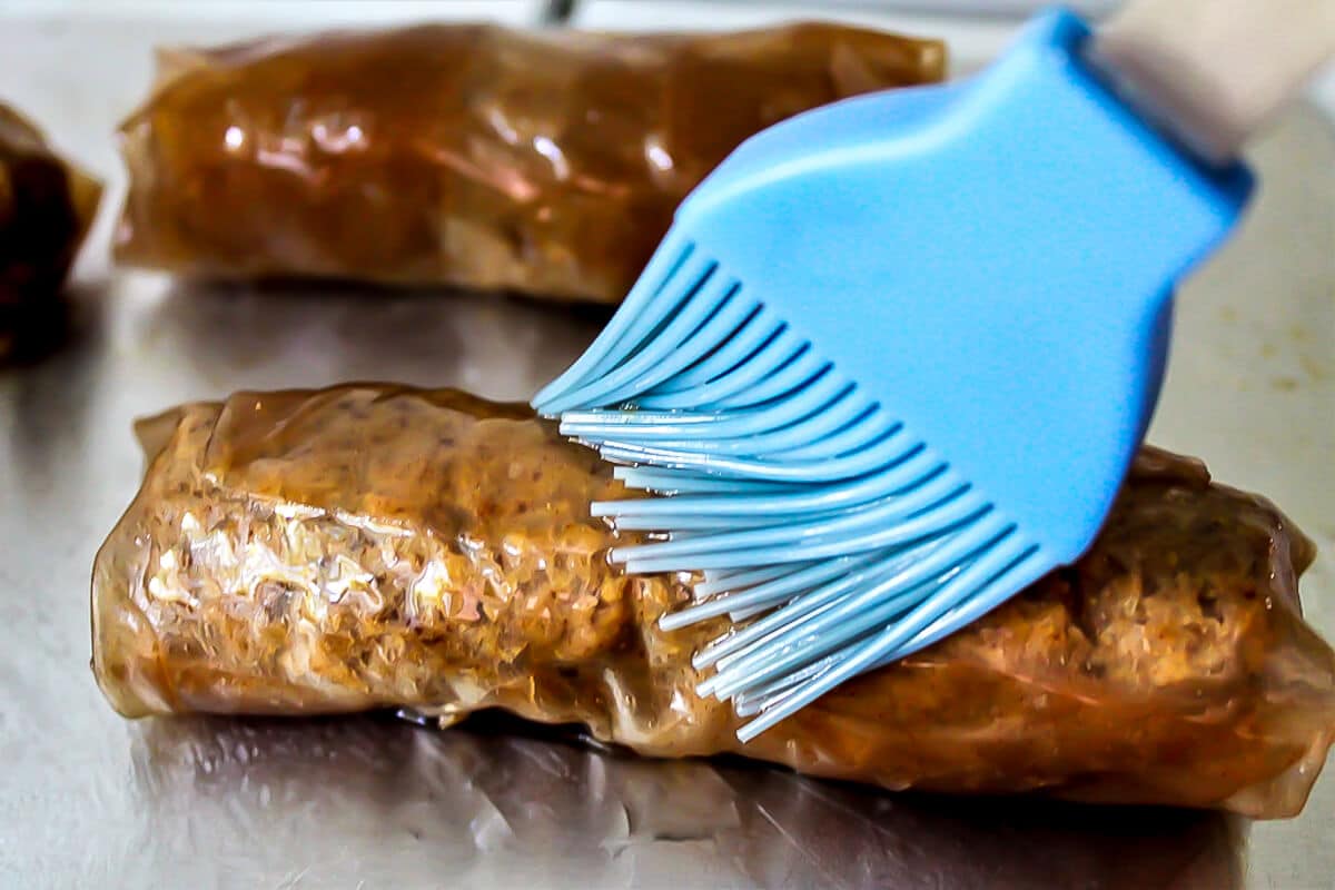 Brushing the vegan sausage with oil before cooking.