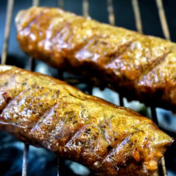 Two gluten-free vegan sausage links cooking on a grill.