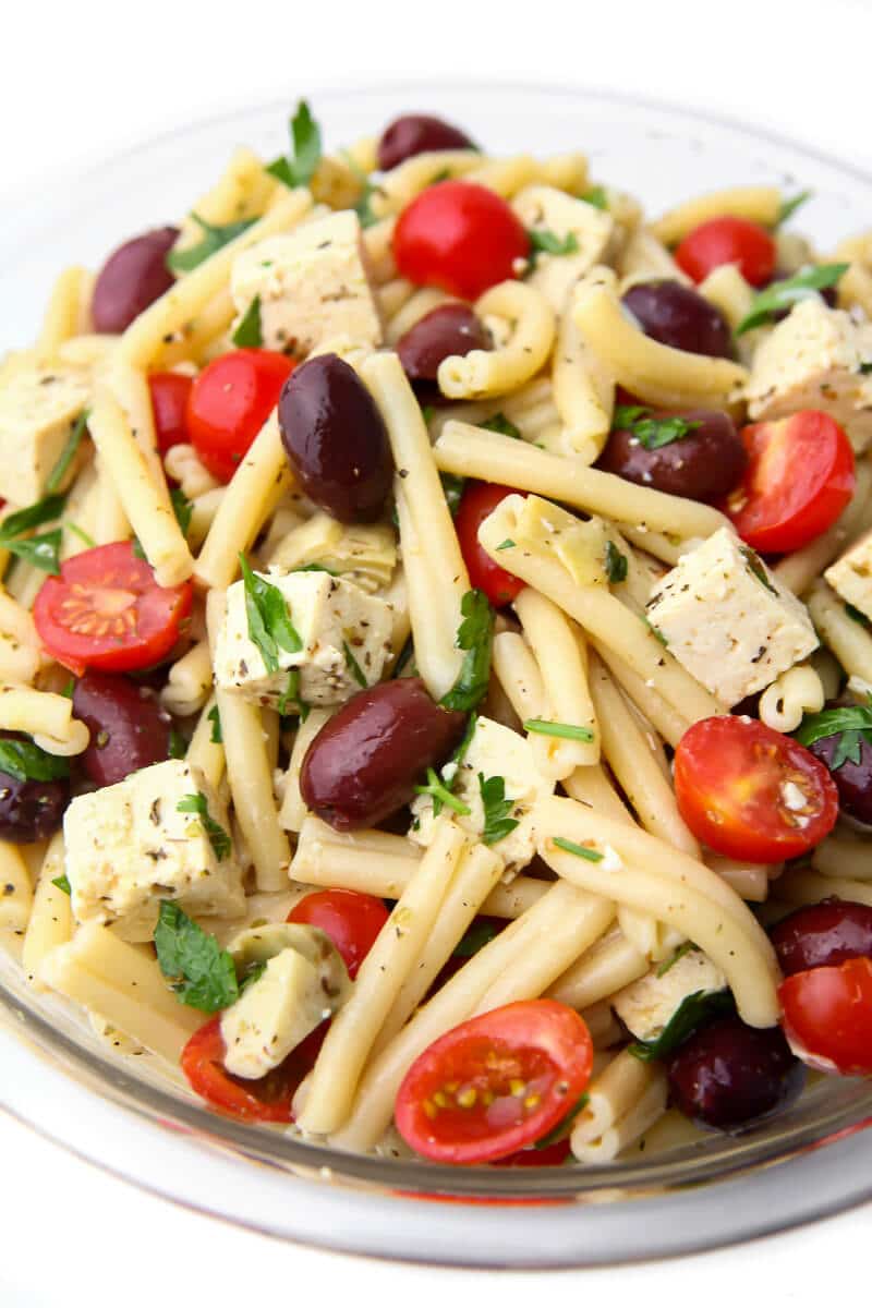 A top view of a vegan pasta salad with cherry tomatoes, parsley, tofu feta, and kalamata olives.