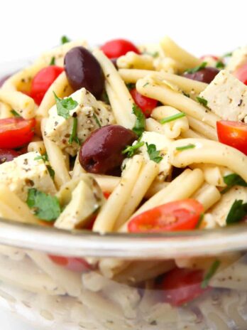 A bowl of vegan Greek pasta salad with a white background.
