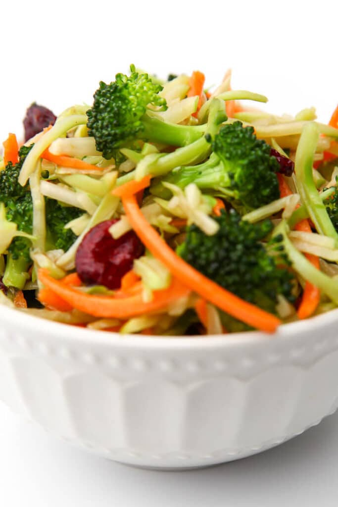 A white bowl filled with vegan broccoli salad with cranberries and shredded carrots. 