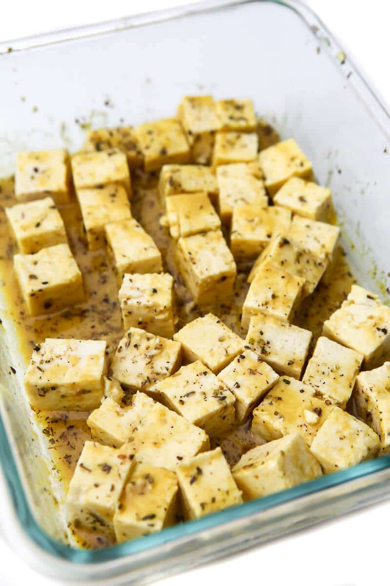 A shallow glass dish filled with tofu marinating in the feta marinade. 