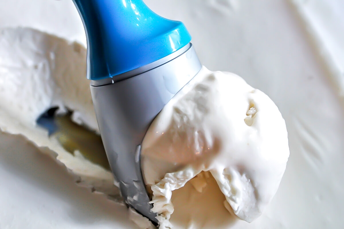 Scooping up aquafaba ice cream with a blue ice cream scoop.