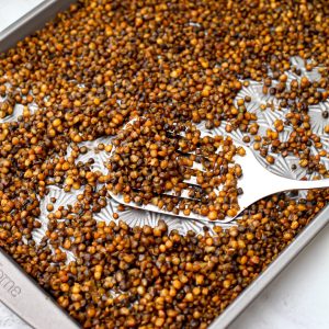 A sheet pan filled with roasted lentils being scooped up with a spatula.