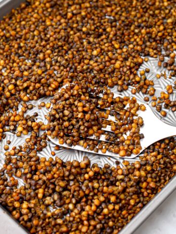 A sheet pan filled with roasted lentils being scooped up with a spatula.