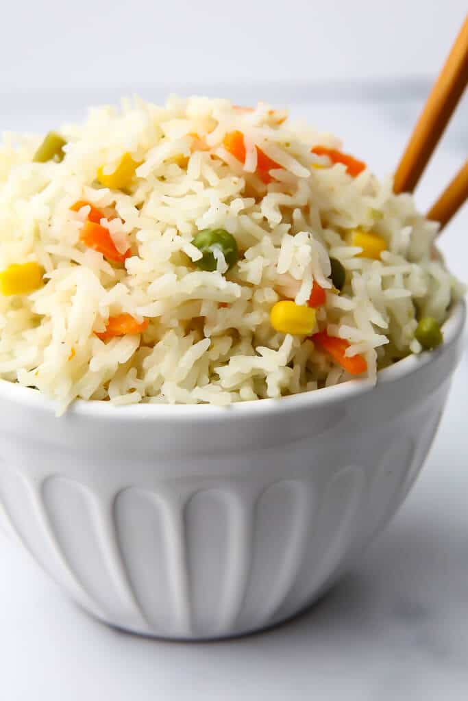 A white bowl filled with coconut rice made with mixed veggies and green curry.