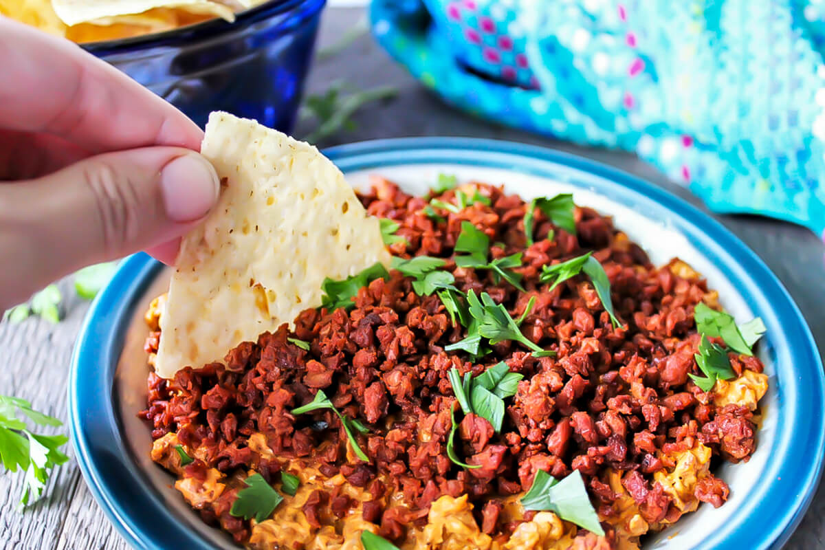 A corn chip being dipped in a bowl of Soyrizo dip.