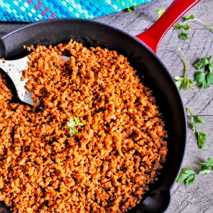 Homemade vegan Soyrizo in a red iron skillet being stirred with a spatula.