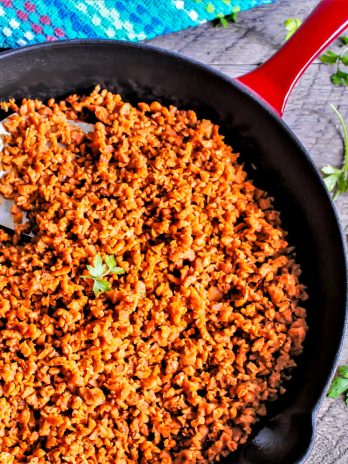 Homemade vegan Soyrizo in a red iron skillet being stirred with a spatula.