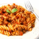 Vegan Bolognese pasta served on a white plate with a fork on the side.