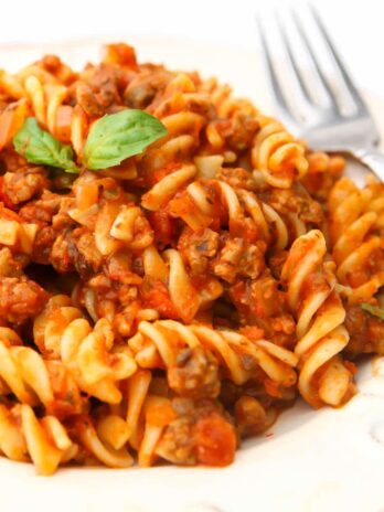 Vegan Bolognese pasta served on a white plate with a fork on the side.
