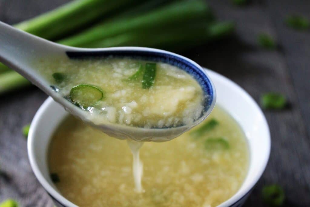 A close up spoonful of vegan egg drop soup in an authentic Chinese bowl and spoon.