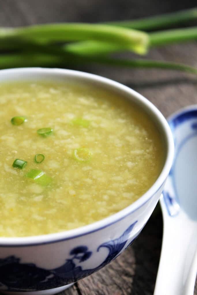 Vegan egg drop soup in a white bowl with green onions behind it.