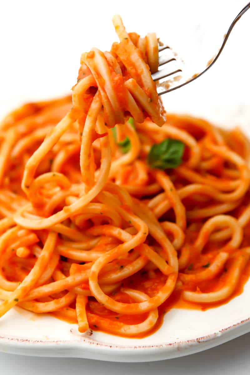 Spaghetti loaded on a fork over a plate full of pasta and oven roasted tomato sauce.
