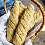 A bread basket with 4 gluten-free vegan breadsticks with a blue napkin behind it.