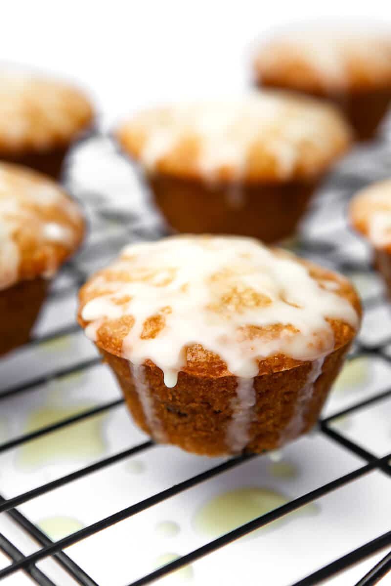 Cranberry orange muffins on a cooling rack with orange glaze dripping off of them.